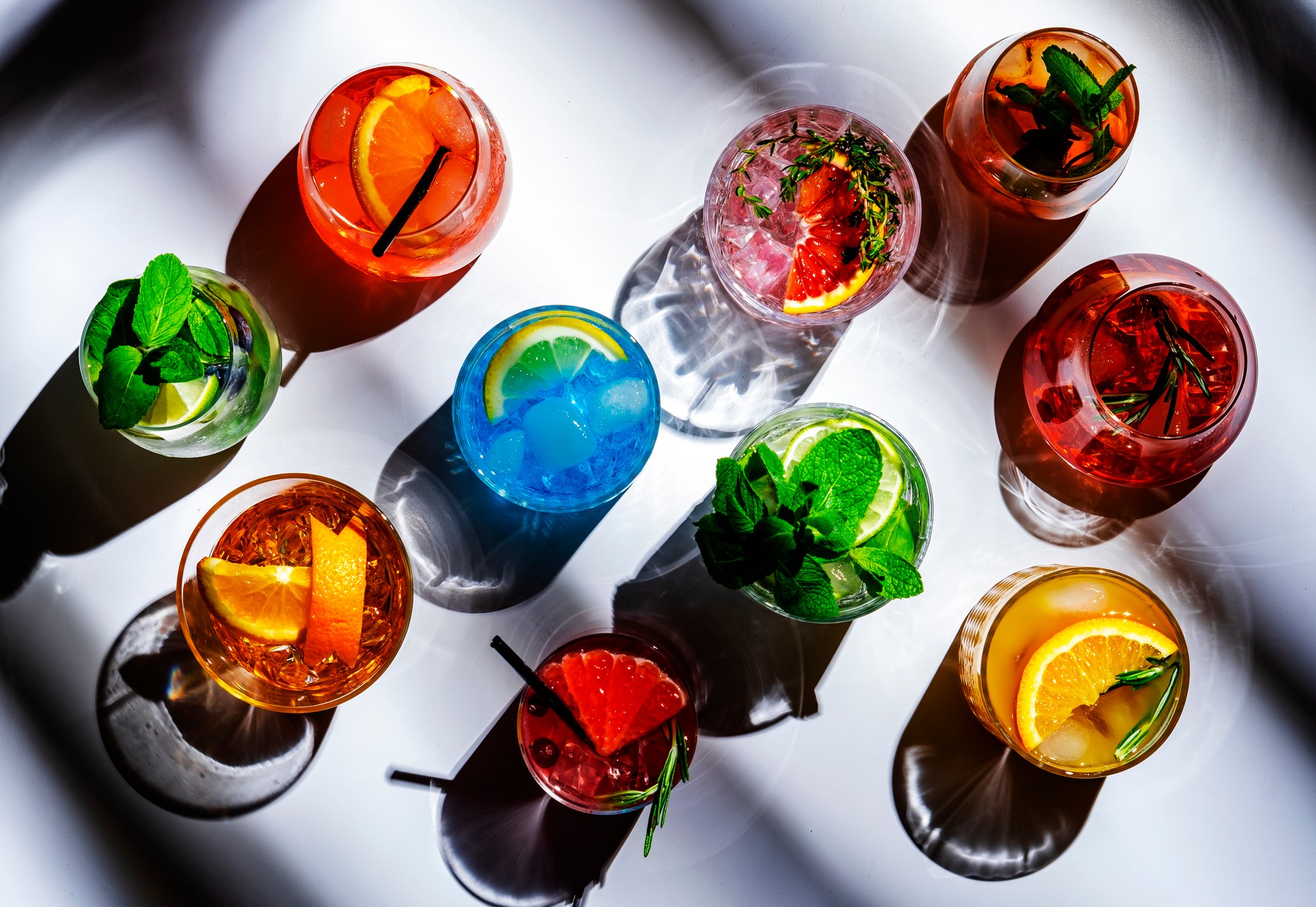 Summer alcoholic cocktails. Assortment of colorful strong and low beverages. White background, hard light, top view